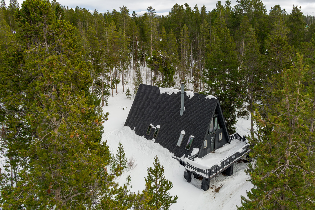 Aerial view of the A-frame alone in a clearing of pines, deep snow all around.