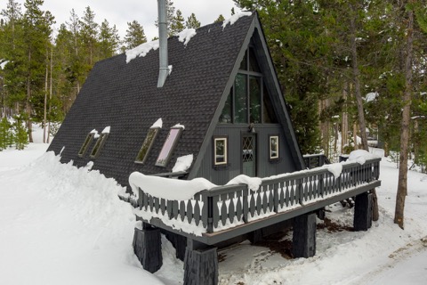 The A-frame's snowy roofline and railing in winter.