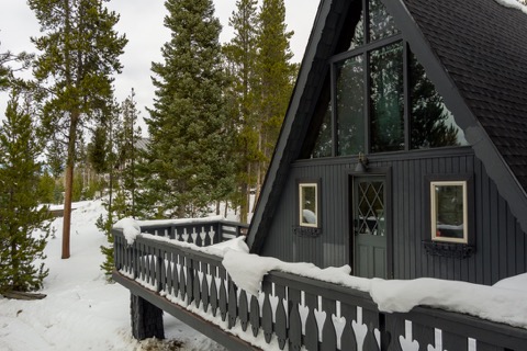 The A-frame and its deck railing among tall pines.